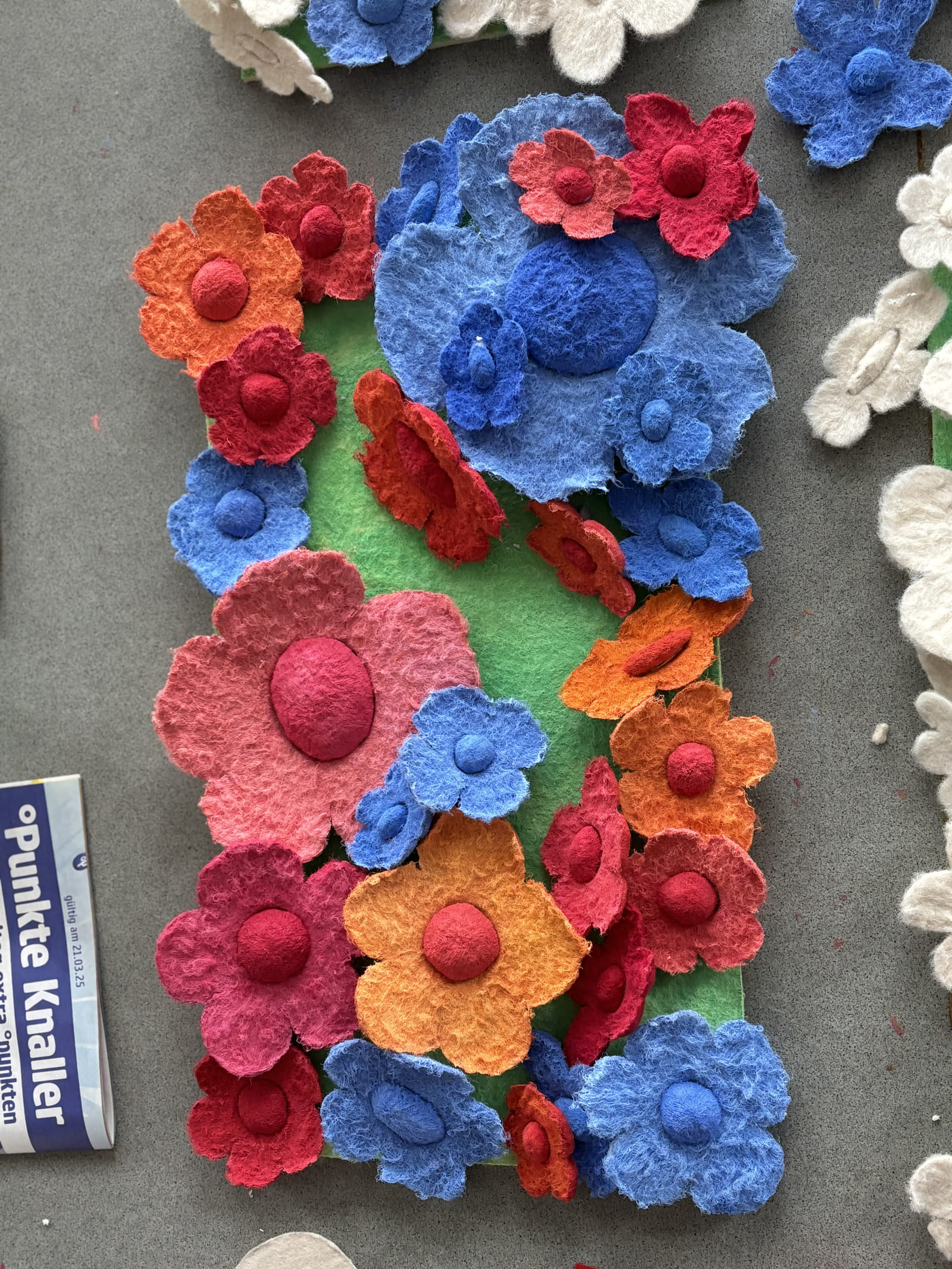 Farbige Filzblüten mit gewölbten Mitten auf einer grünen Tafel am Arbeitstisch.