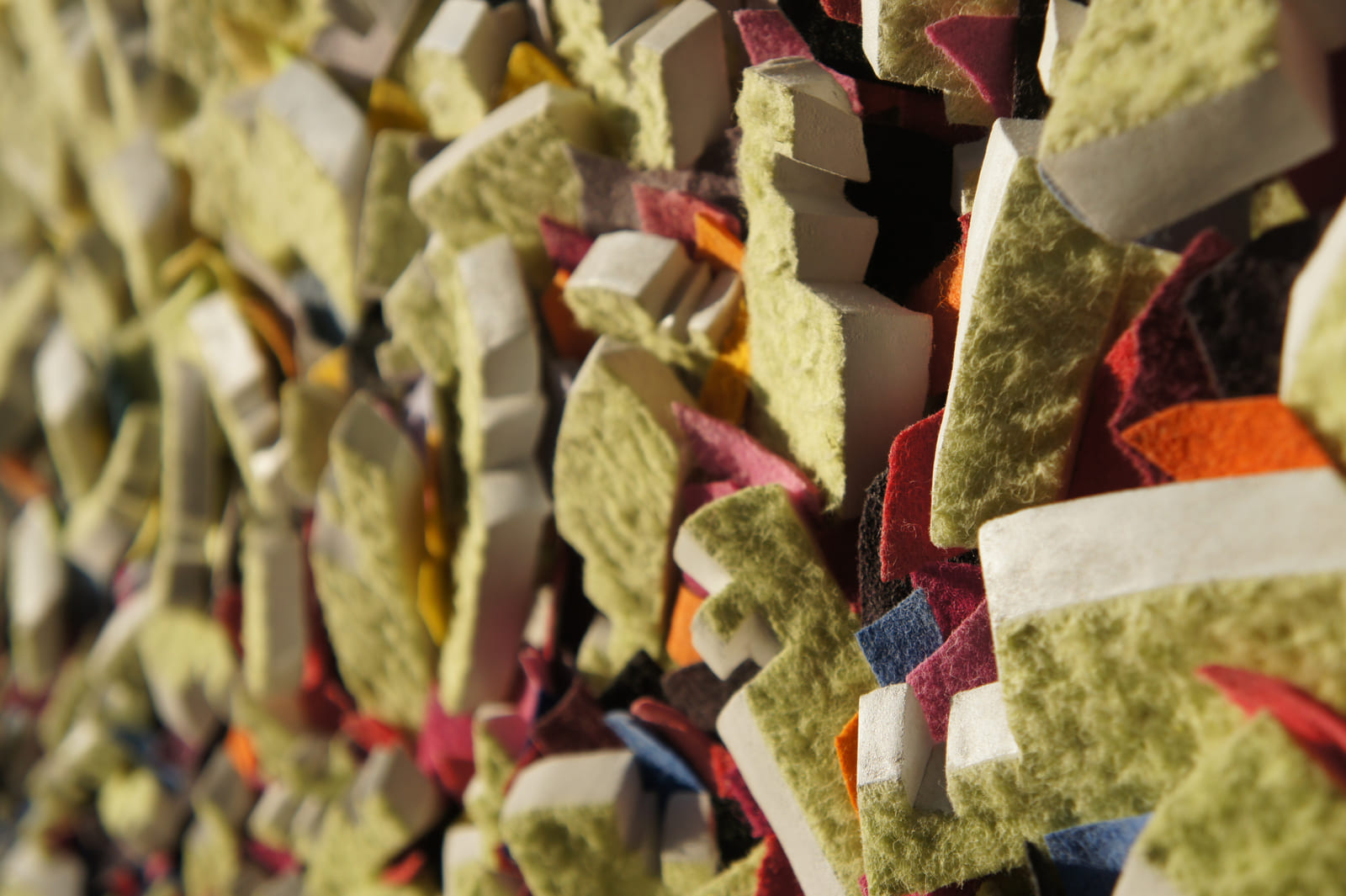 Detail eines gelben Filzreliefs mit weißen Seitenflächen und farbigen Zwischenlagen.