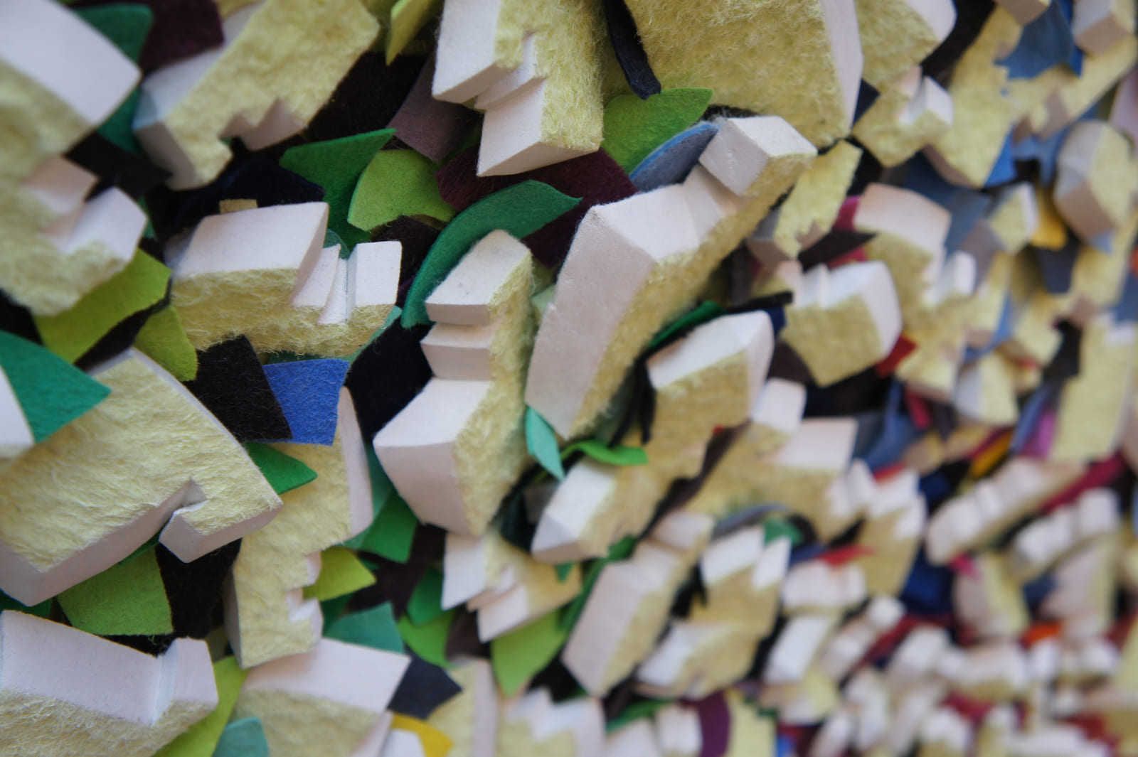 Detail eines gelben Filzreliefs mit grünen und blauen Zwischenlagen.