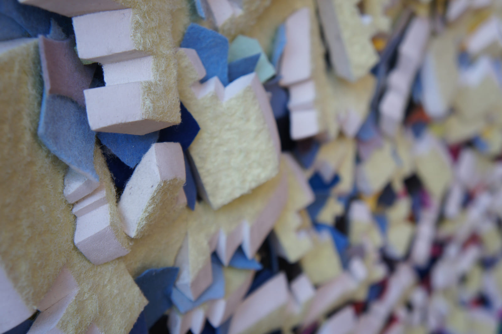 Detail eines gelben Filzreliefs mit blauen Zwischenlagen und weißen Schnittflächen.