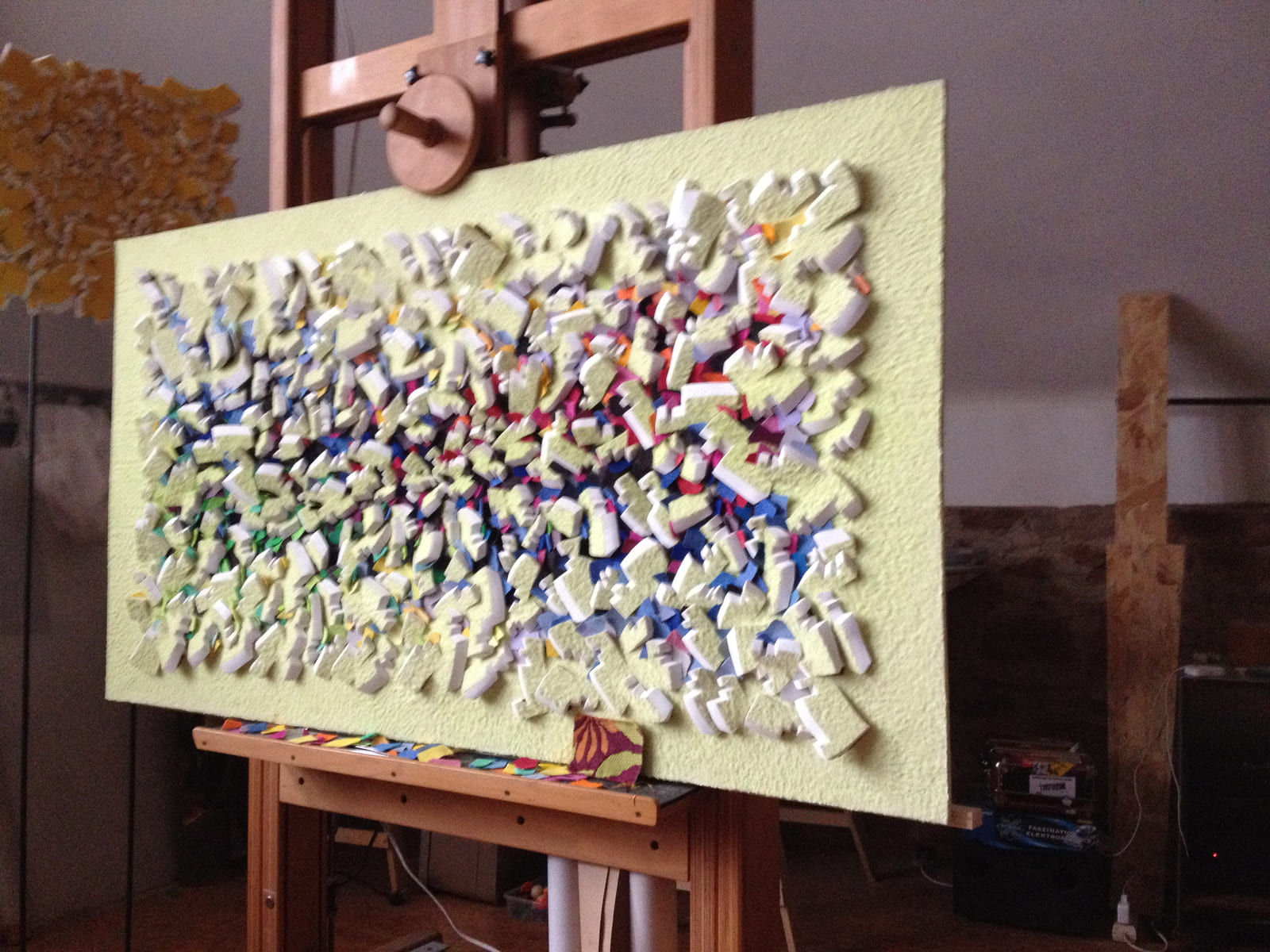Gelbes Relief mit farbigen Zwischenlagen im Atelier auf einer Staffelei.