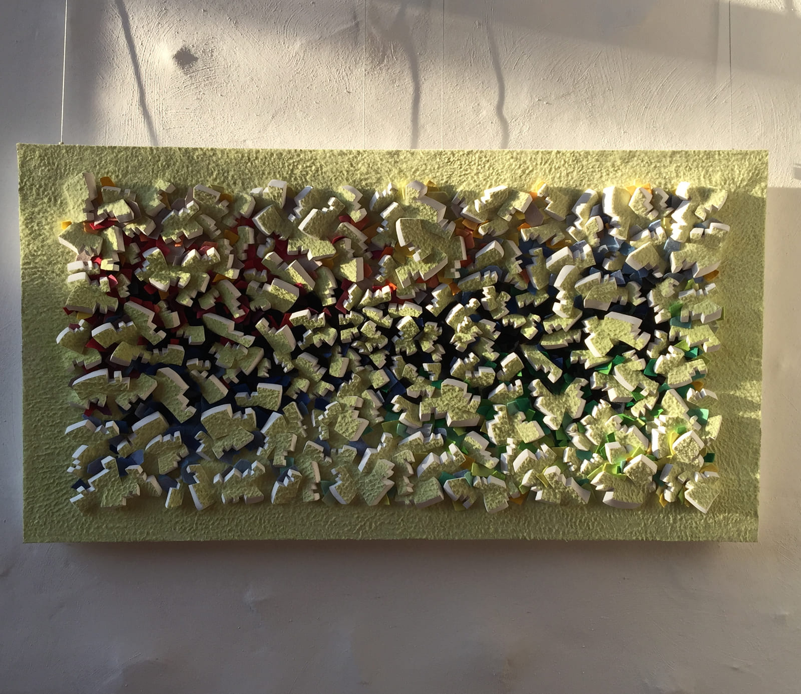 Gelbes Relief frontal an einer hellen Wand bei seitlichem Sonnenlicht.
